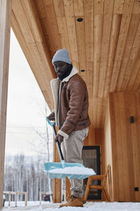 Man holding shovel with snow on porch outside house