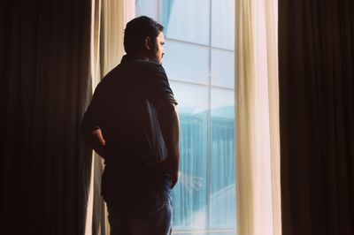 Rear view of man standing against window