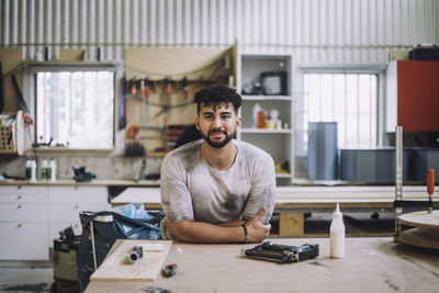Portrait of smiling carpenter leaning on workbench