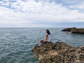 Side view of woman meditation on rock against sea