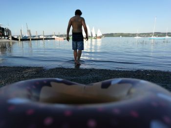 Rear view of shirtless man in sea against sky