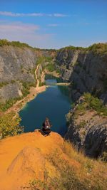 High angle view of man crouching on cliff against lake
