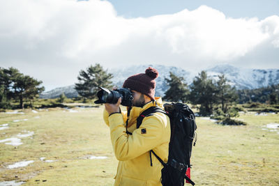 Young man with yellow jacket and backpack taking pictures on the mount