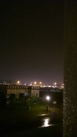 Illuminated buildings by river against sky at night