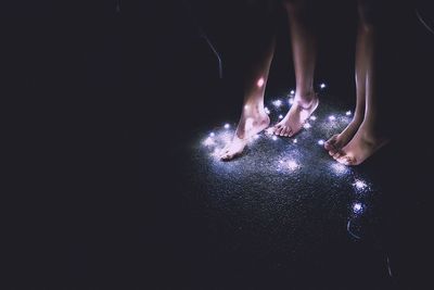 Low section of women standing by fairy lights on road at night