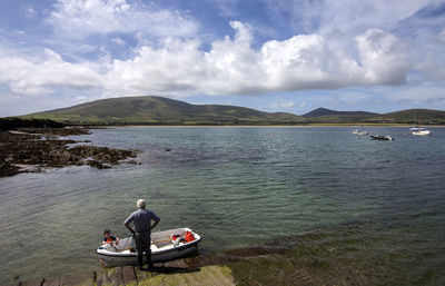 High angle view of grandfather and grandson standing by boat at lake against cloudy sky