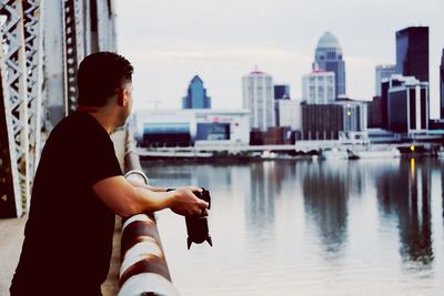 Man standing with camera by sea against sky