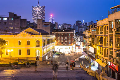 People in illuminated city against clear sky at night