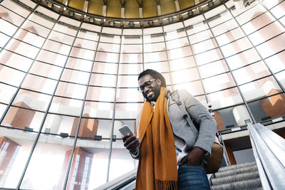 Smiling man using mobile phone while standing against ceiling