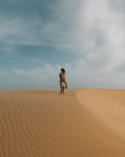 Man standing on sand dune in desert against sky