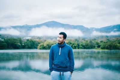 Young man standing in front of lake against sky