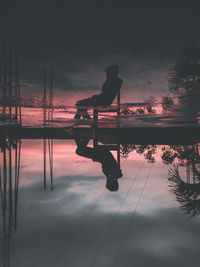 Silhouette man standing by lake against sky during sunset