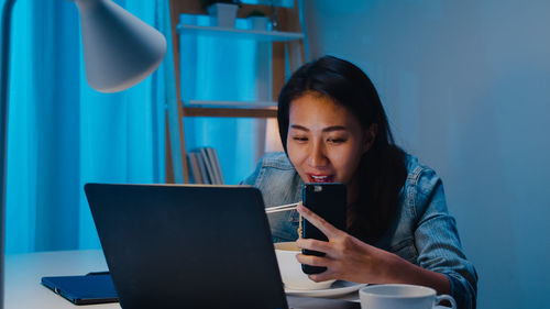 Mid adult woman using mobile phone while sitting on table