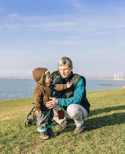 Full length of grandfather and granddaughter on field by sea against sky