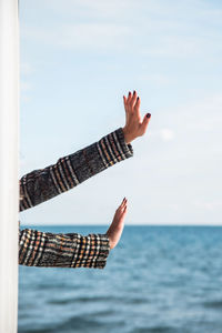 Cropped hands of woman over sea against sky
