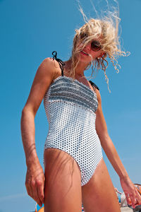 Low angle view of young woman in swimwear against clear blue sky