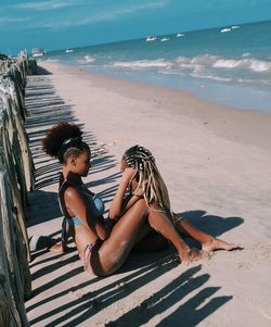 Female friends sitting at beach against sky