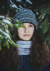 Portrait of a beautiful girl with curly brown hair against a background of fir branches.
