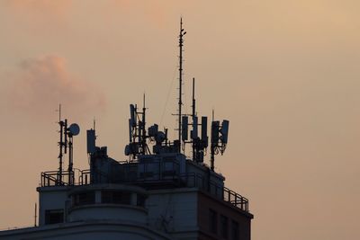 Low angle view of antennas on building against sky during sunset