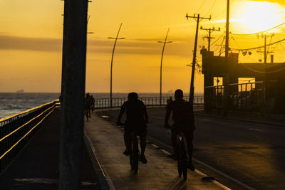 Rear view of people walking on road at sunset