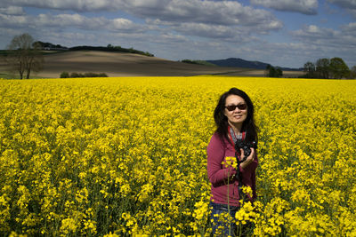 Beautiful young woman standing in field with yellow flowers in background