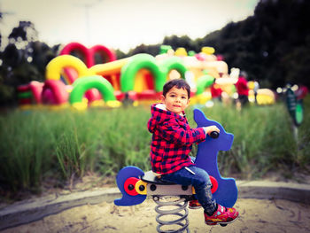 Side view of cute boy sitting on spring ride at playground