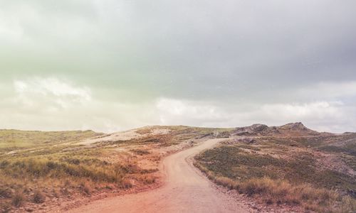 Dirt road amidst field against sky