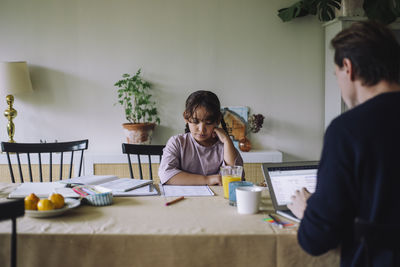 Girl studying with father using laptop while sitting at dining table in home