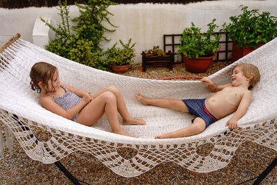 Cute barefooted little sister and brother lying in hammock and having fun during summer holidays