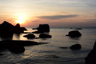 Silhouette rocks in sea against sky during sunset