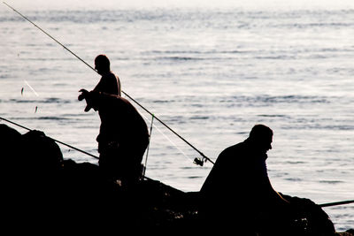 Silhouette man fishing in sea against sky