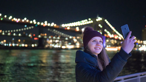 Portrait of smiling young woman standing against illuminated sky at night