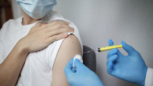 Doctor in mask holding ampoule with coronavirus vaccine, nurse holding syringe to make injection