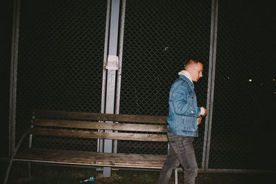 Side view of man walking by chainlink fence