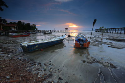 Boats moored on beach against sky during sunset