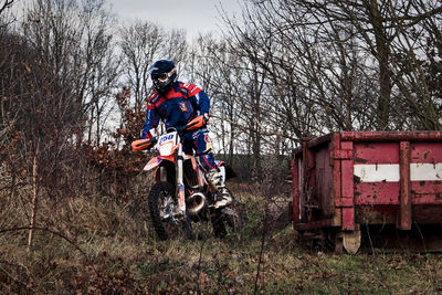 Person riding motocross on field against bare trees