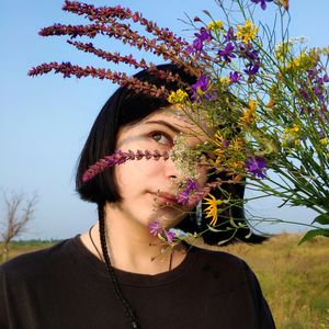 Portrait of beautiful woman with pink flowers against sky