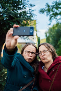 Smiling twins puckering while taking selfie with smart phone