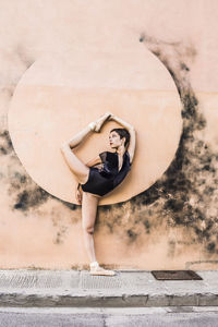 Full length of ballerina standing on one leg while dancing against wall