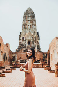 Portrait of young woman standing outside historic building against sky