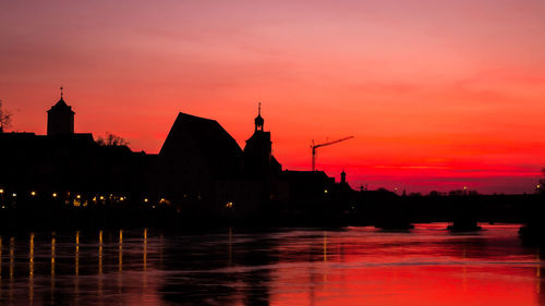 Silhouette of buildings at waterfront during sunset