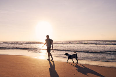 Silhouette woman walking at beach against sky during sunset