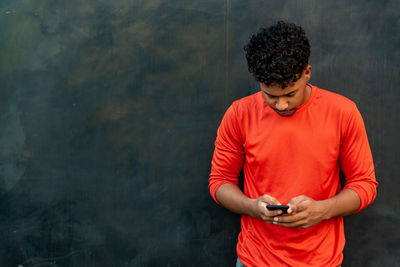 Man using mobile phone while standing against wall