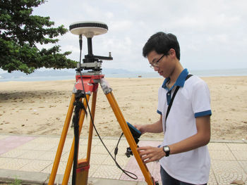 Vietnamese geodetic engineer surveyor doing measurements with gnss satellite receiver on the beach