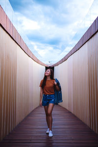 Full length portrait of young woman standing against wall