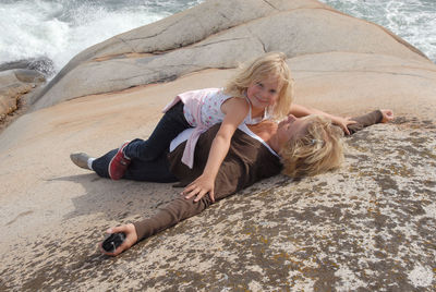 Full length of mother and daughter lying on rock formation at sea shore