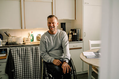 Cheerful mature man sitting on wheelchair in kitchen at home