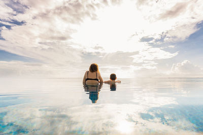 Mother and son into a infinity pool. back view.
