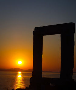 Silhouette built structure by sea against orange sky