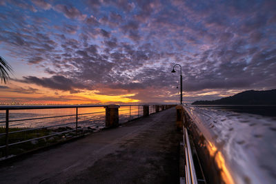 Road by sea against sky during sunset